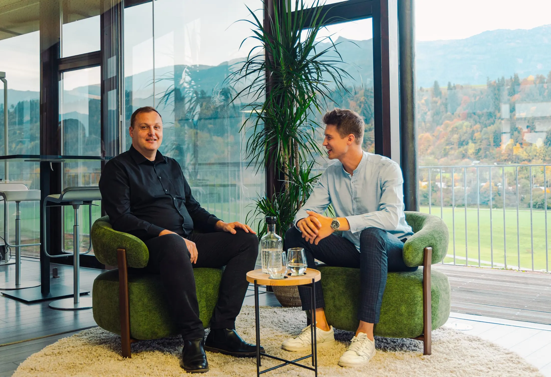 Two Kaino employees talking in green armchairs in front of windows with a mountain view